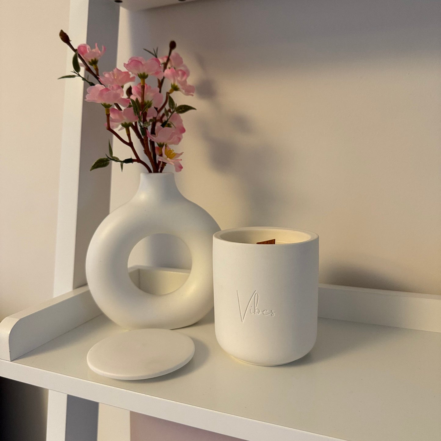 Modern white ceramic candle with a decorative vase containing pink flowers 